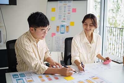 Product development team collaborating on user experience design layouts with an interface flow chart whiteboard in the background.